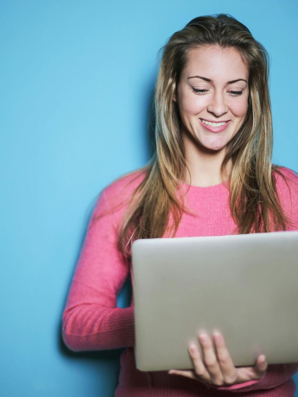 Smiling person in a pink sweater using a laptop against a blue background
