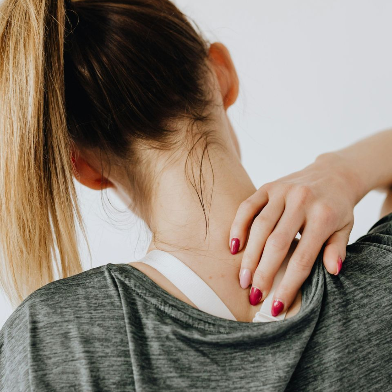 Person massaging the back of their neck in a gray shirt, with a hand reaching over the shoulder