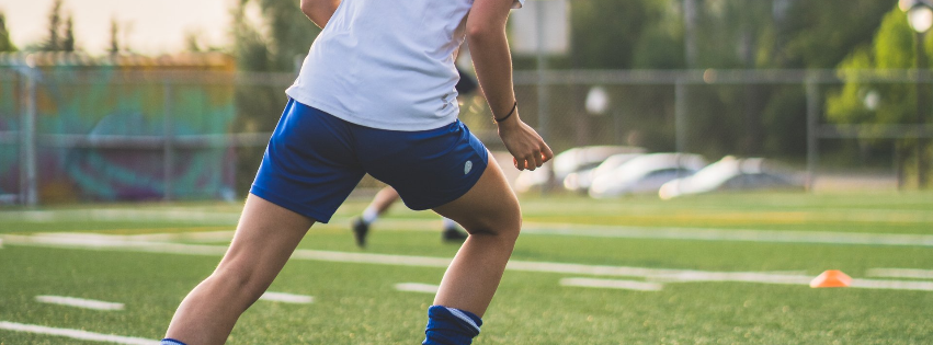 Person running on a grassy sports field wearing a white shirt and blue shorts