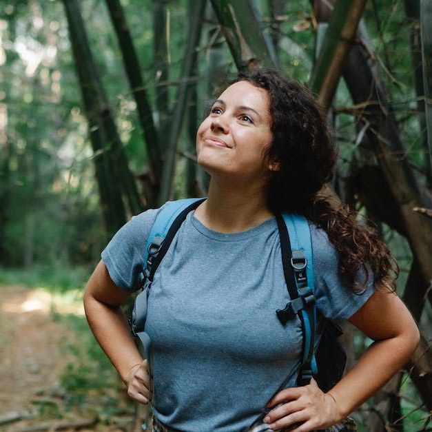 Woman with backpack smiling in a bamboo forest, hands on hips