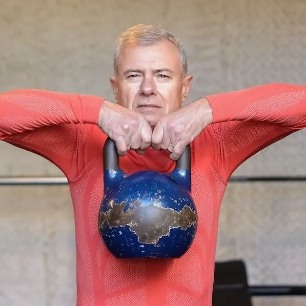 Man holding a blue kettlebell at chest height, wearing a red long-sleeve shirt.