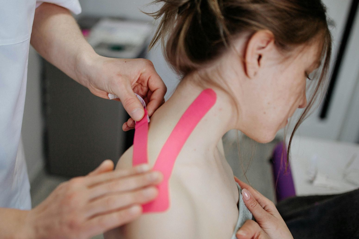 Pink kinesiology tape being applied to a person’s neck and shoulder during treatment