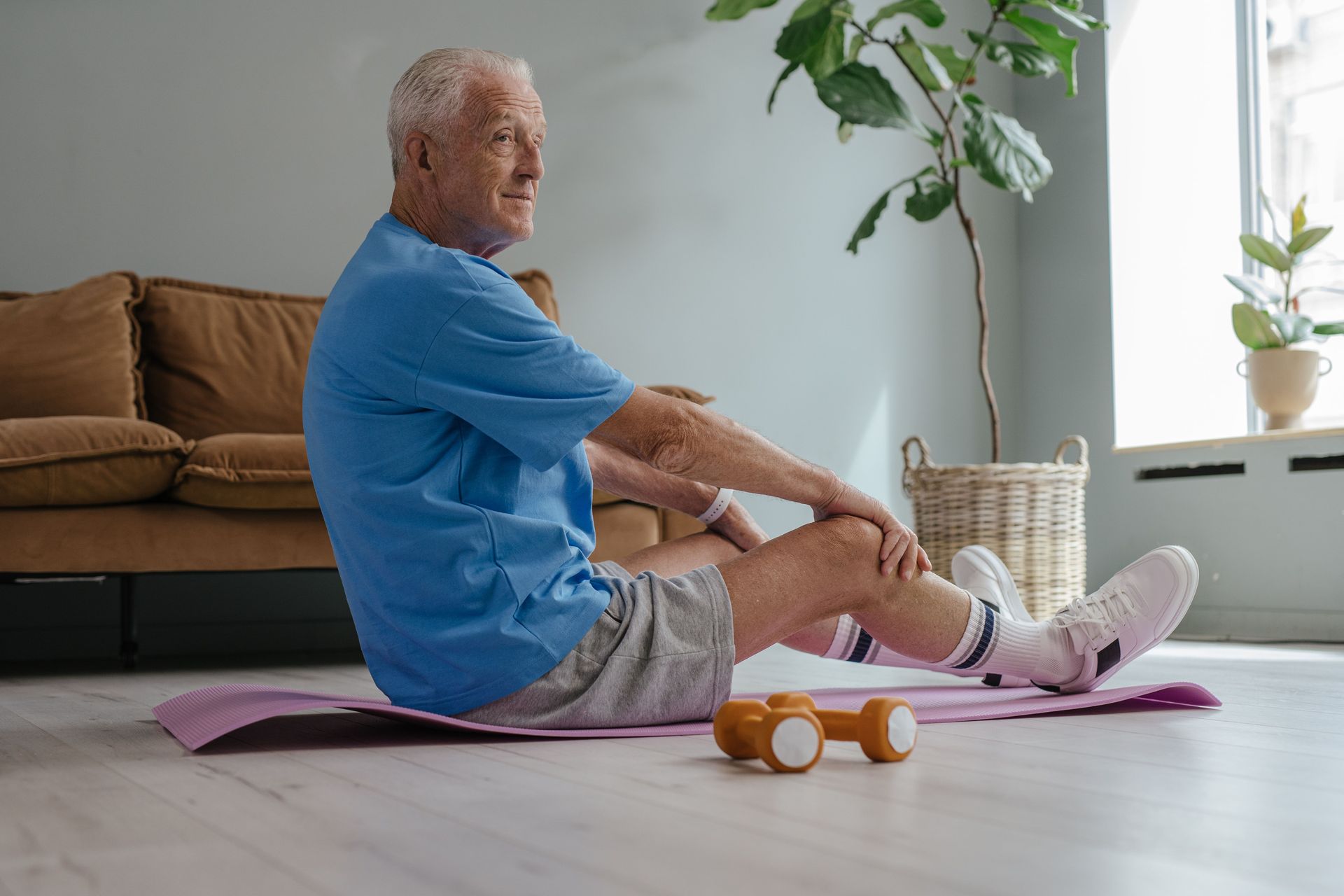 Person stretching on a yoga mat beside dumbbells in a bright living room