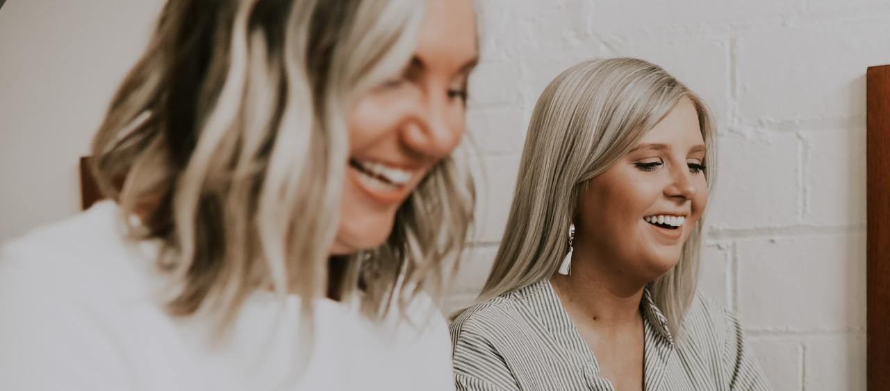 Two women working on laptops and smiling in a bright office