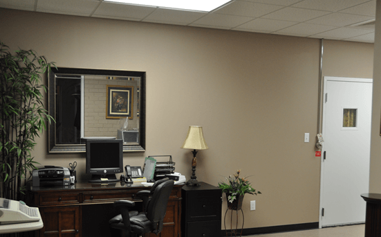 Office with desk, mirror, lamp, and door in a beige-colored room.