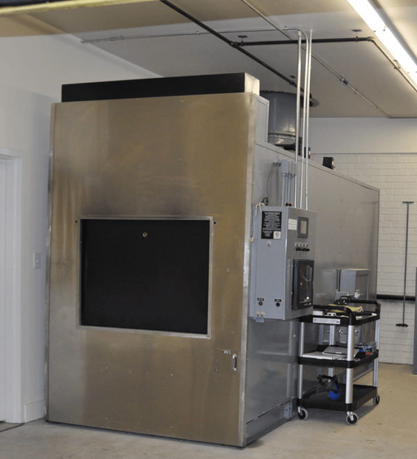 Large stainless steel industrial oven with control panel and cart in a lab setting.