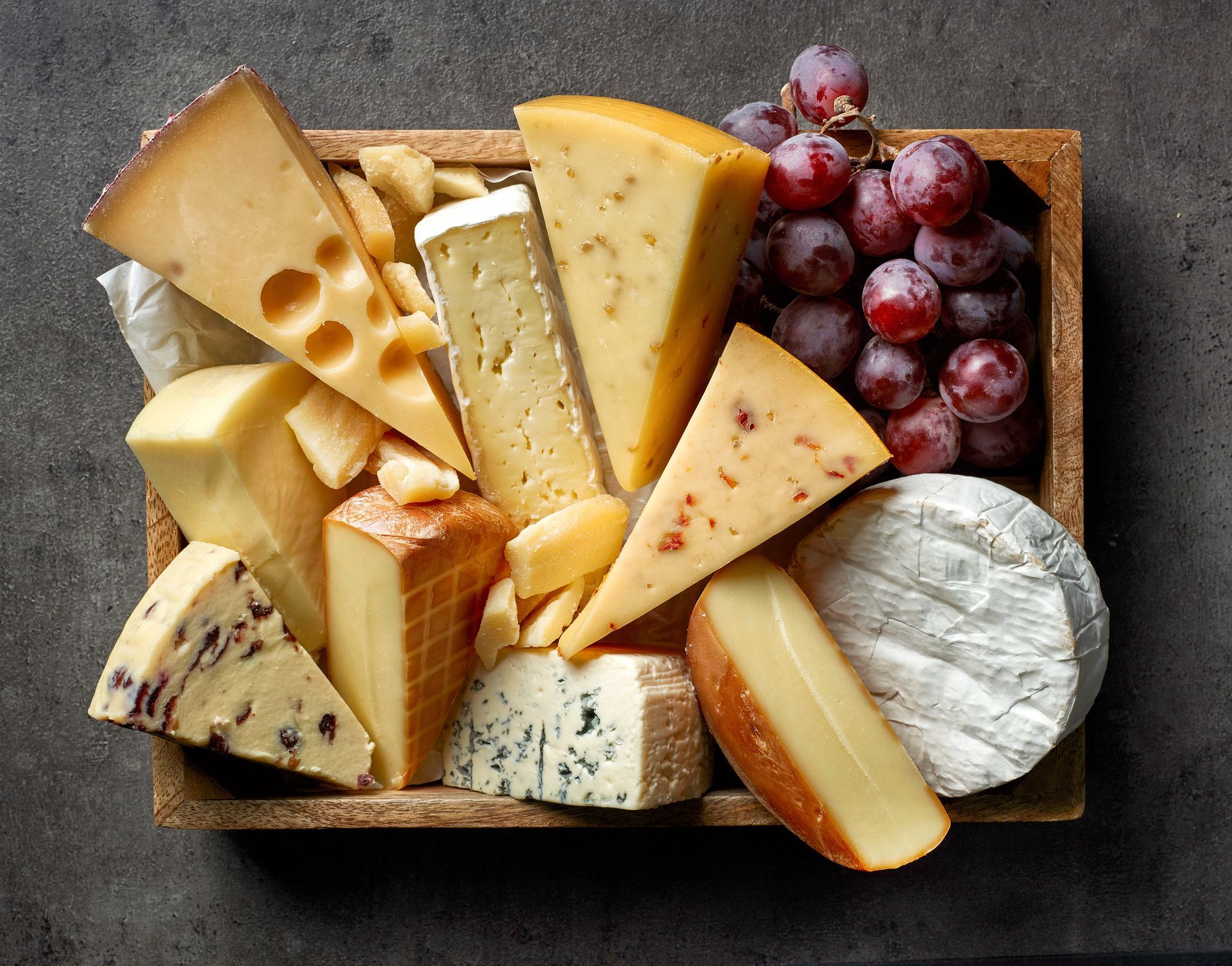 a wooden box filled with different types of cheese and grapes .