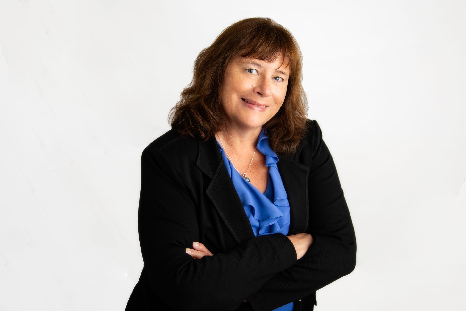 Woman in a black blazer and blue blouse, smiling with arms crossed against a white background