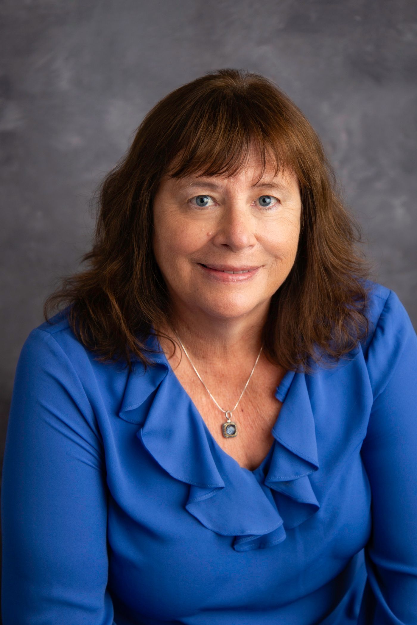 Portrait of a woman in a blue blouse smiling against a gray backdrop