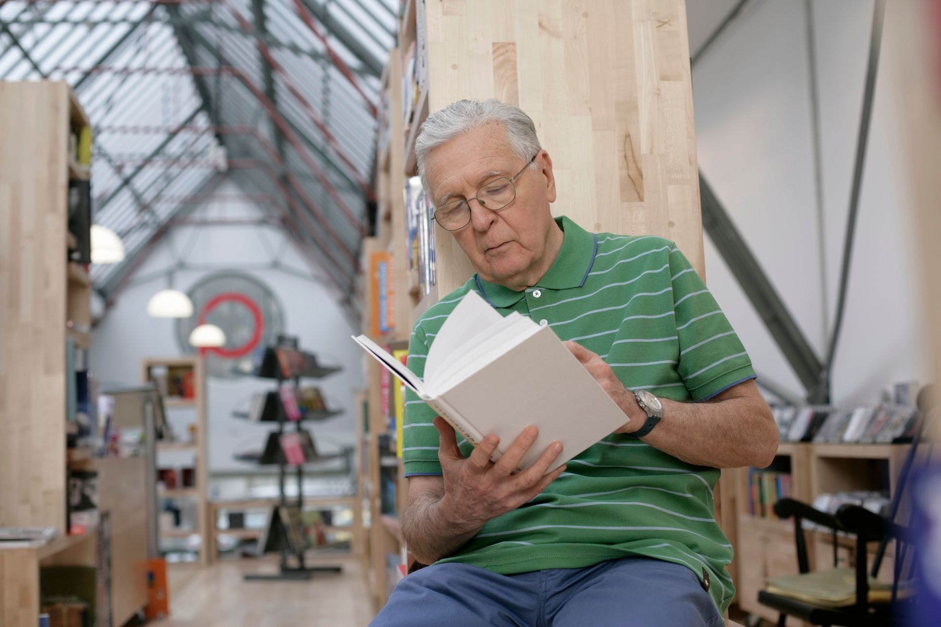 Man in green striped polo reading a book in a bright greenhouse-like space