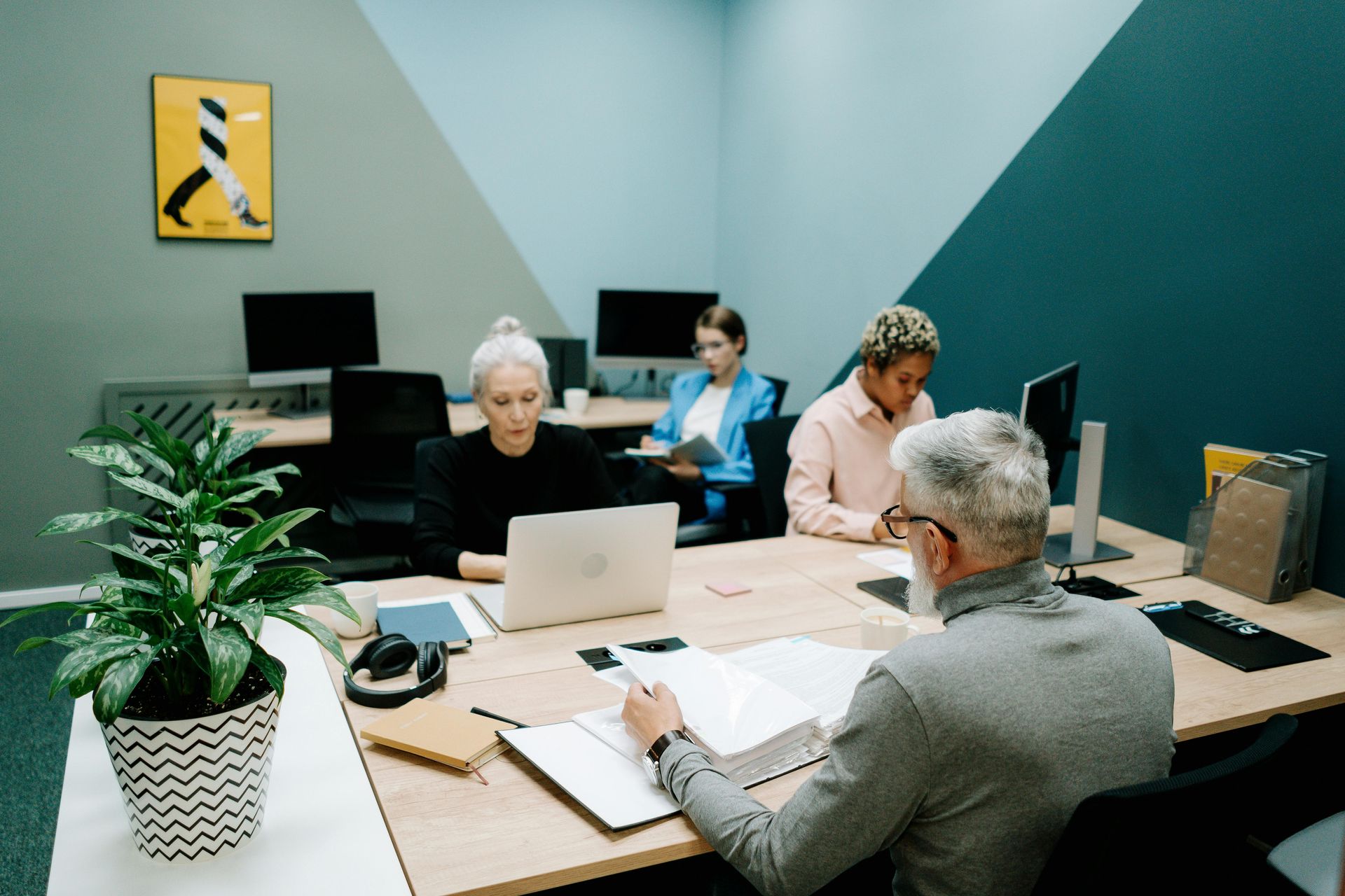 Small office meeting with four people working at desks around a laptop and paperwork.