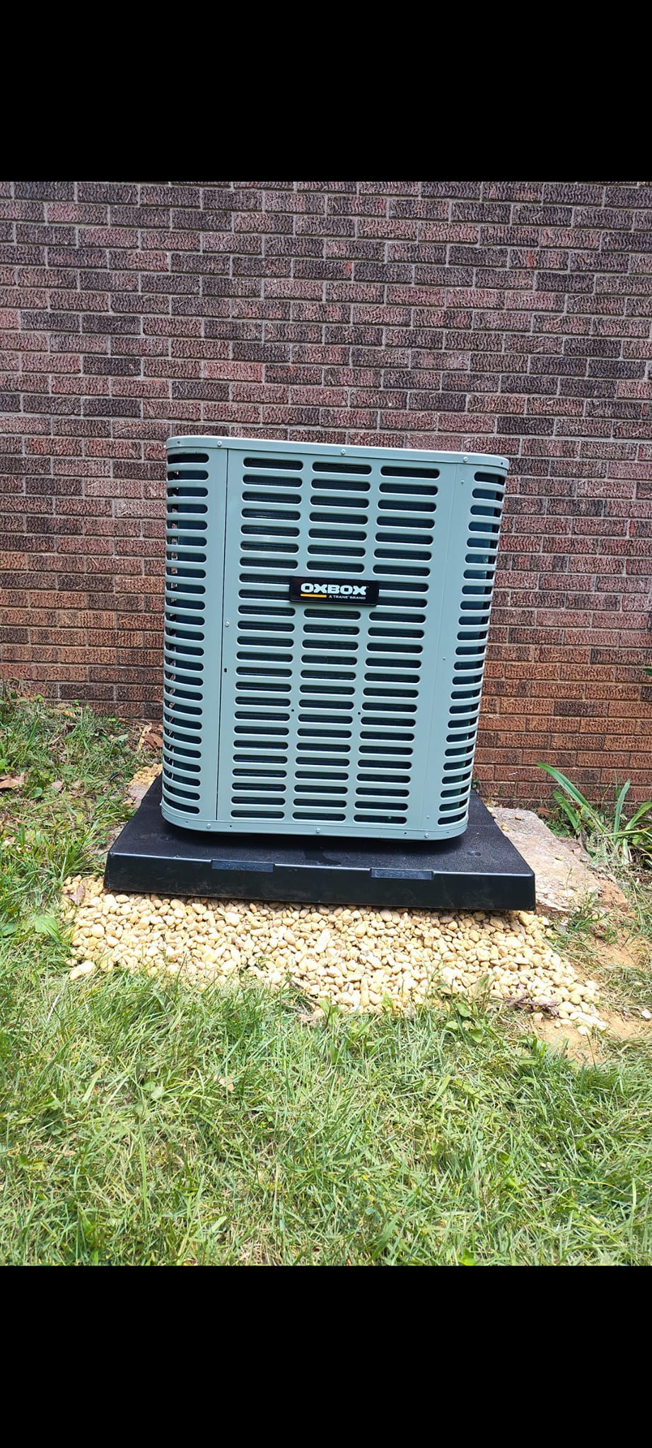 Blue outdoor air conditioning unit on a concrete pad beside a brick wall and grass.