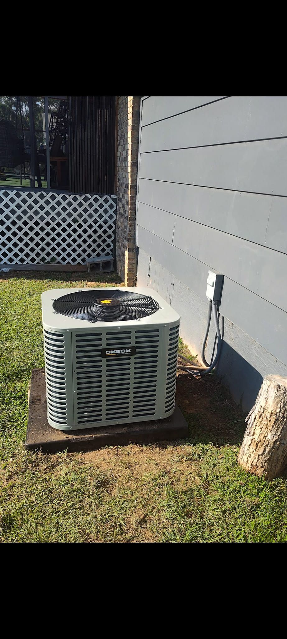 Outdoor air conditioner unit beside a white house wall and lattice fence on a grassy yard