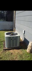 Outdoor air conditioner unit beside a white house wall and lattice fence on a grassy yard