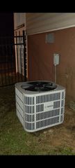 Outdoor air conditioning unit beside a brick house at night, lit by a flash.