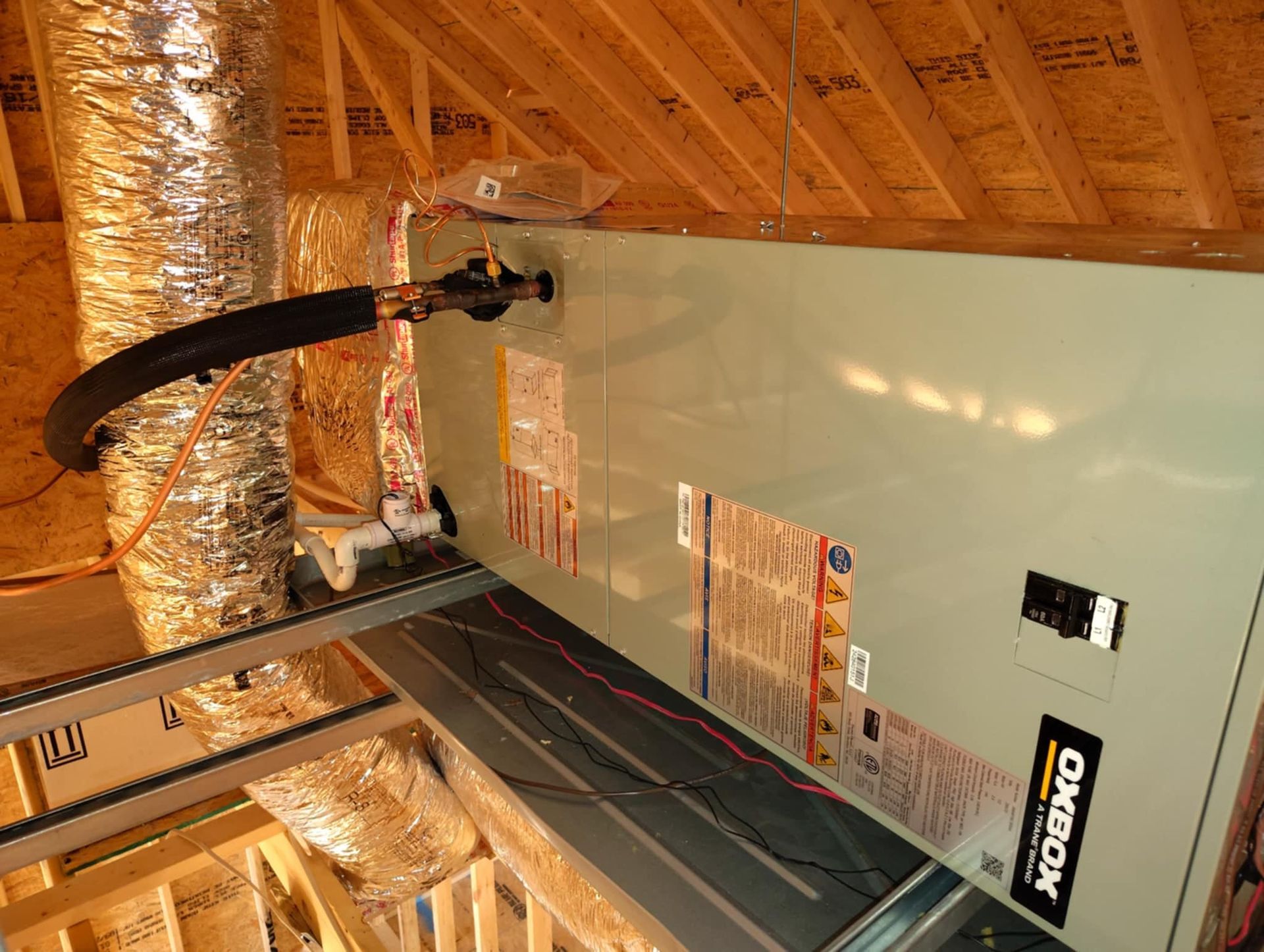 Unfinished attic with insulated walls, exposed rafters, and a curved black cable or duct hanging overhead