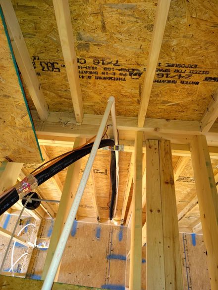Inside a wood-framed attic, a person is pointing a tool at the plywood ceiling sheathing.