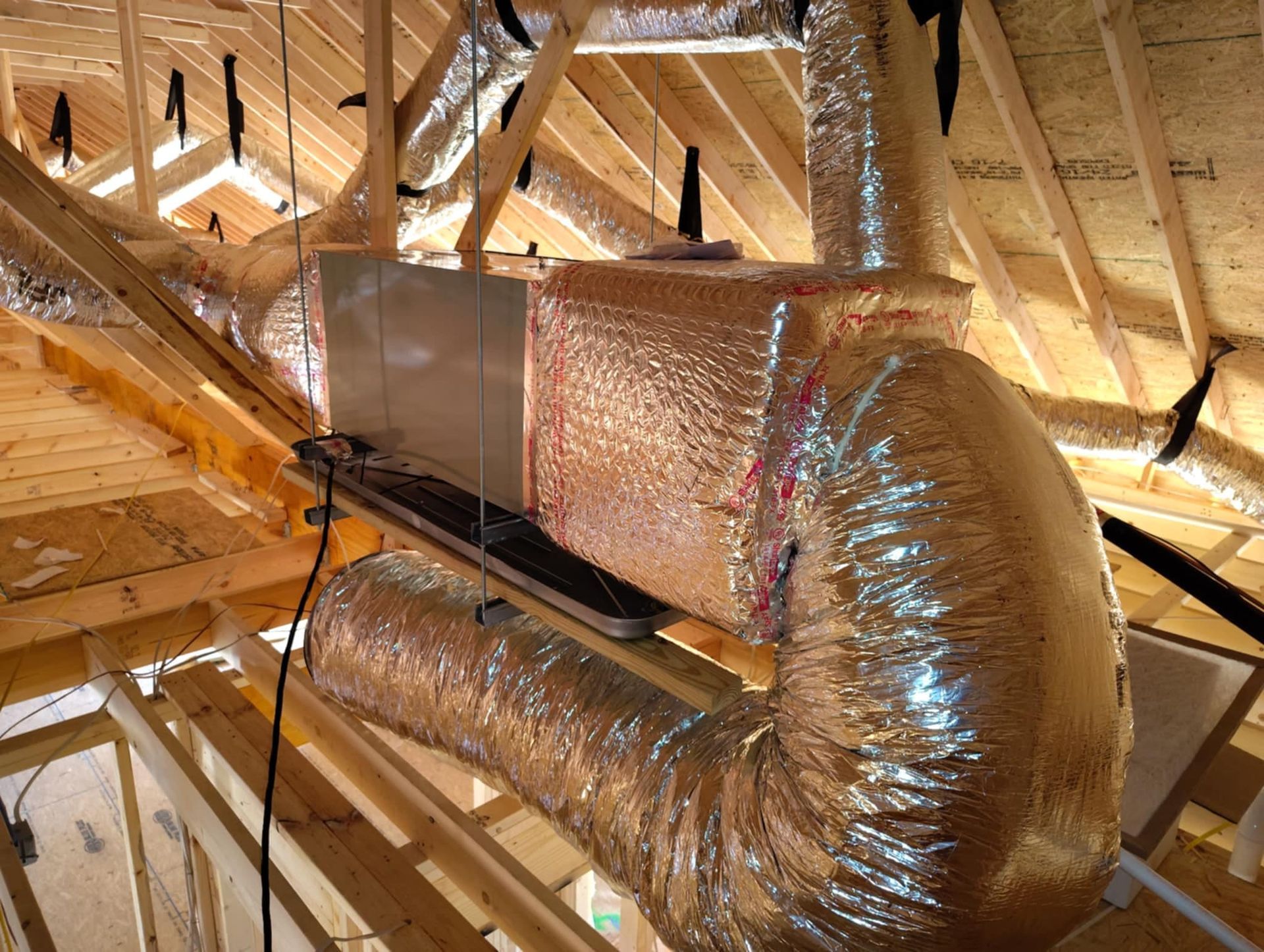 Flexible silver HVAC ducts in an attic with exposed wooden rafters and insulation