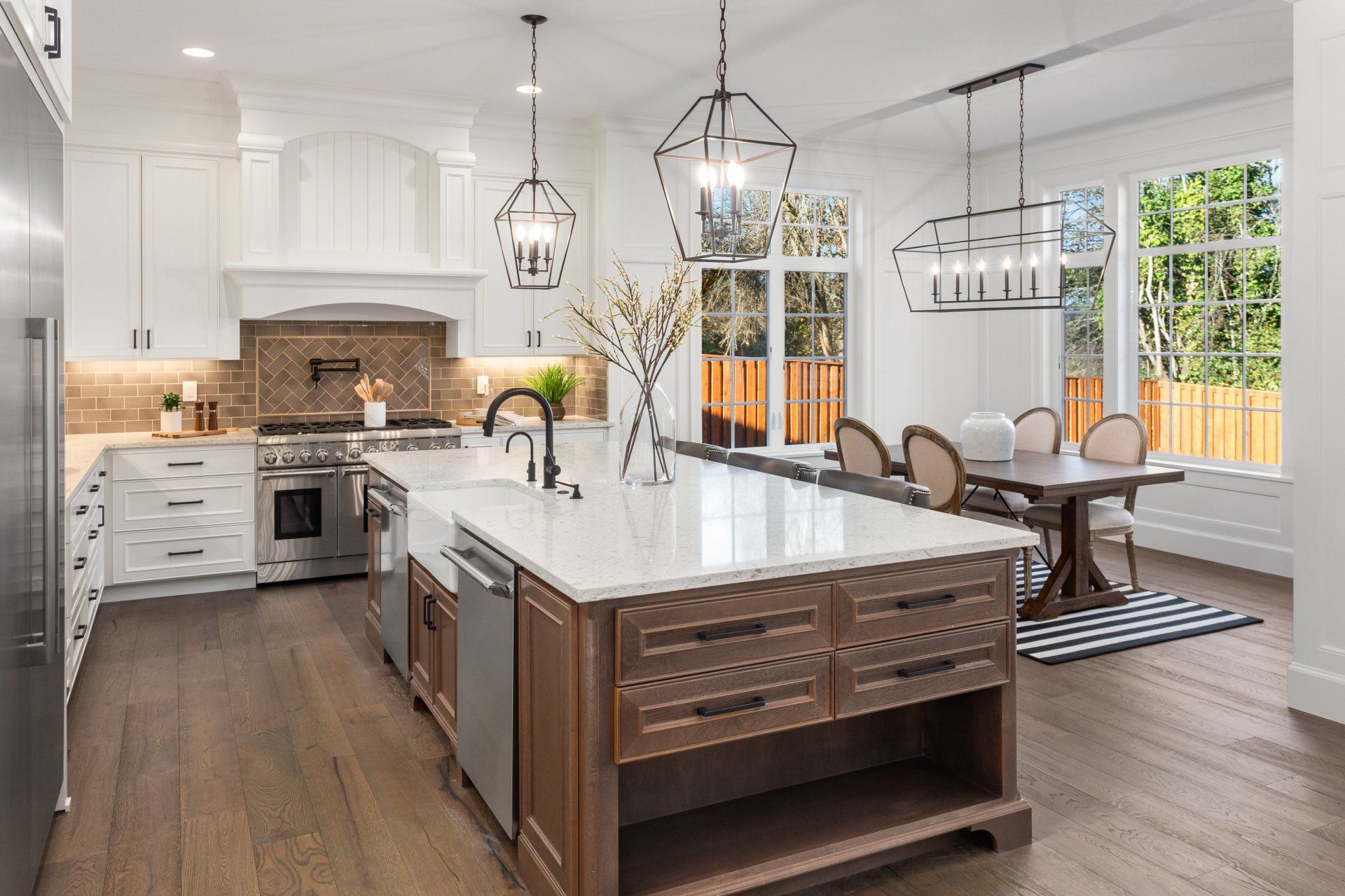 Bright modern kitchen with white cabinets, marble island, and dining area by large windows