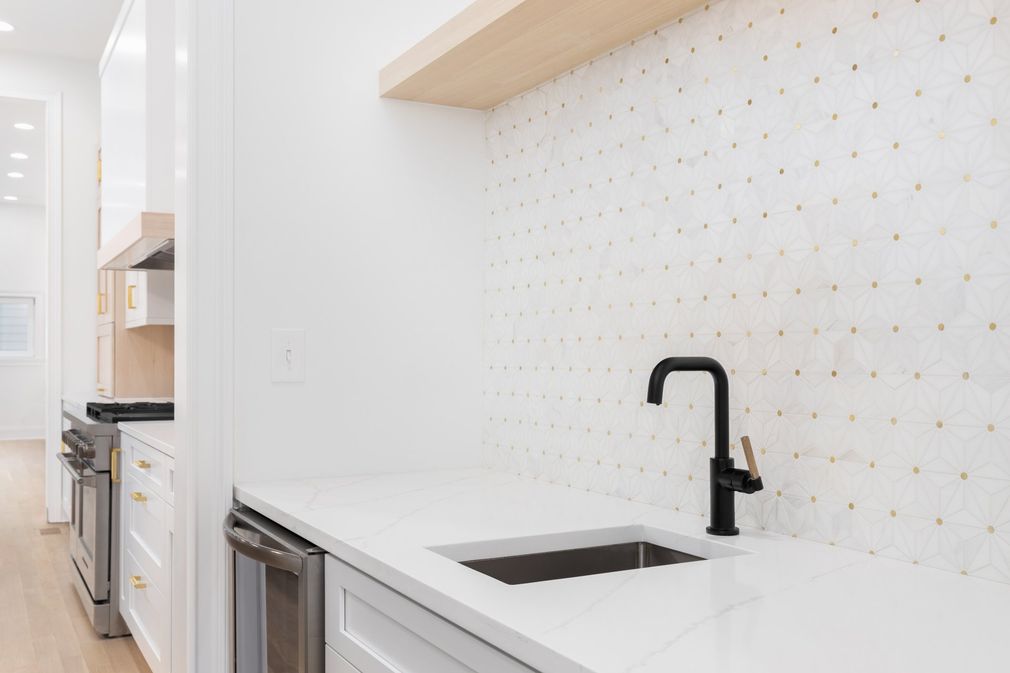 Modern white kitchen with black faucet, white countertop, and light wood shelving