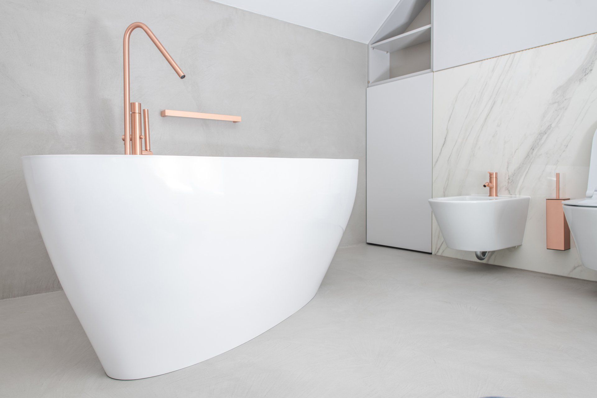 Minimalist bathroom with a white freestanding tub, copper faucet, and wall-mounted sink on a light gray floor