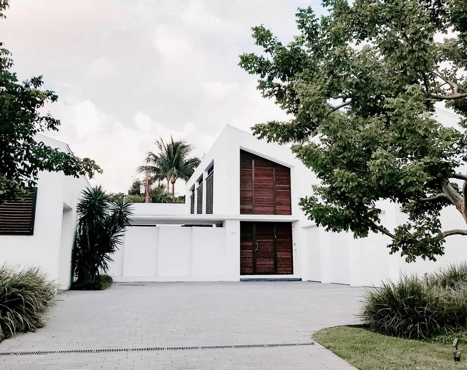 Modern white house with geometric roof, wooden shutters, and trees in front