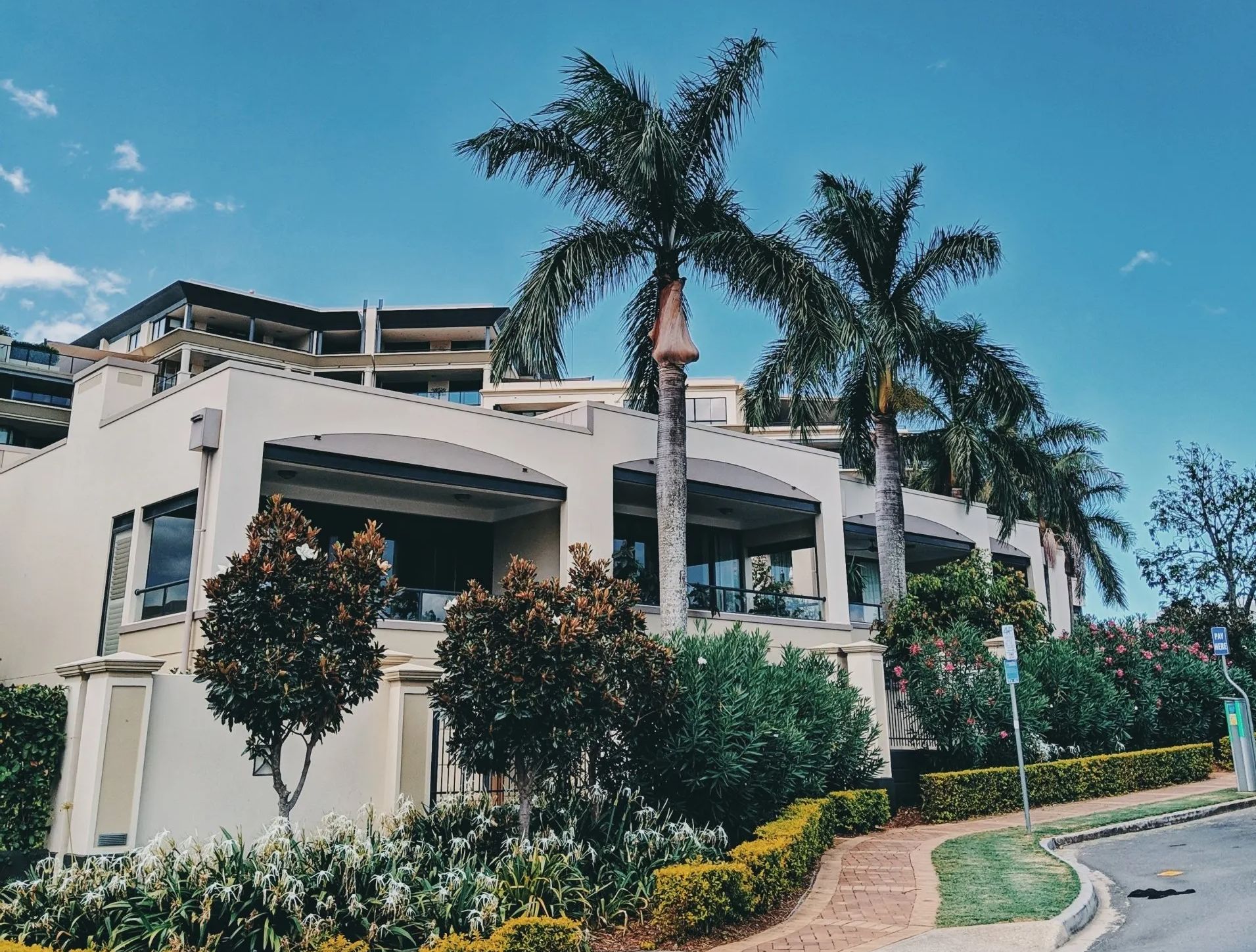 Modern white building with palm trees, landscaped greenery, and a curved driveway under a blue sky