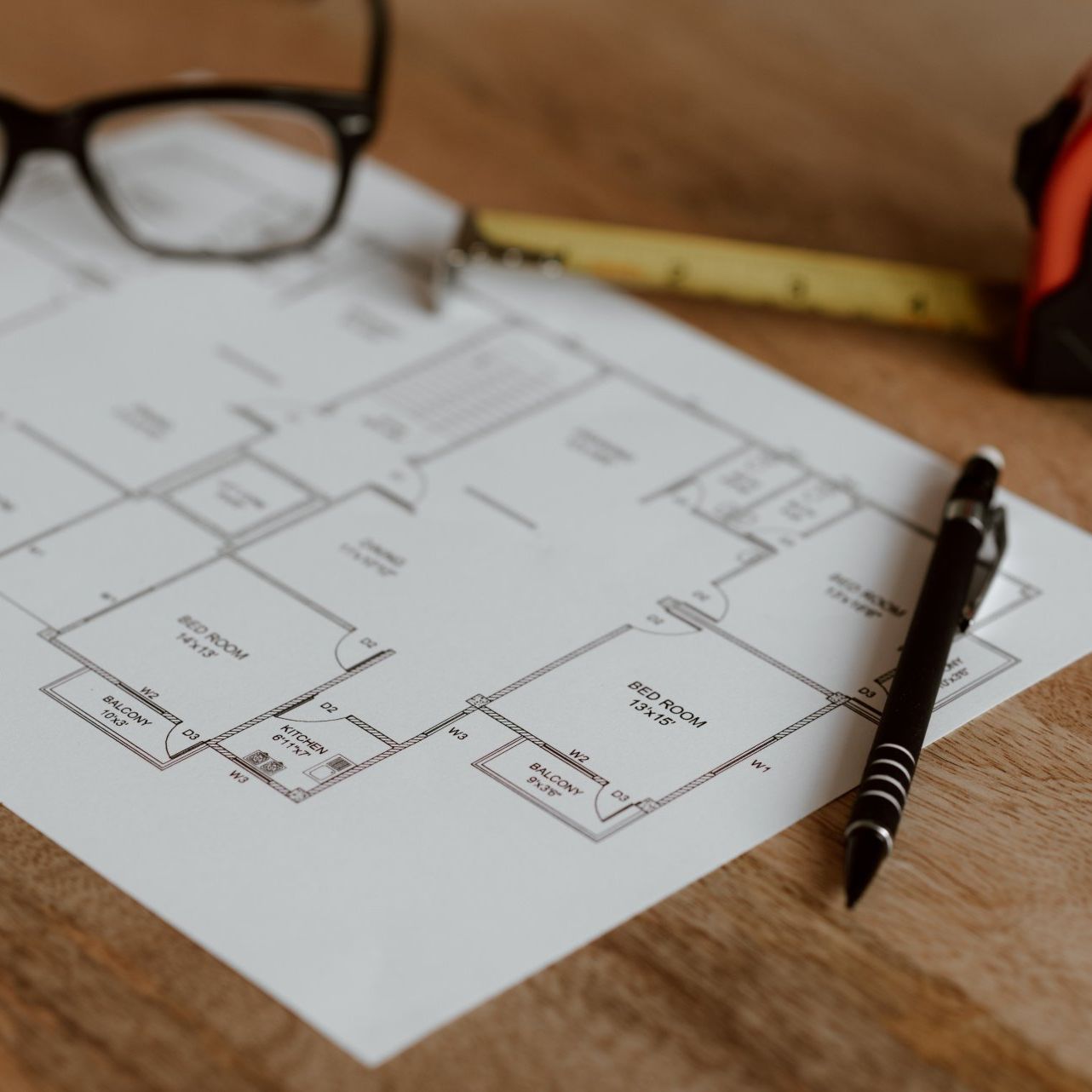 Floor plan on a wooden desk with glasses, ruler, and pen