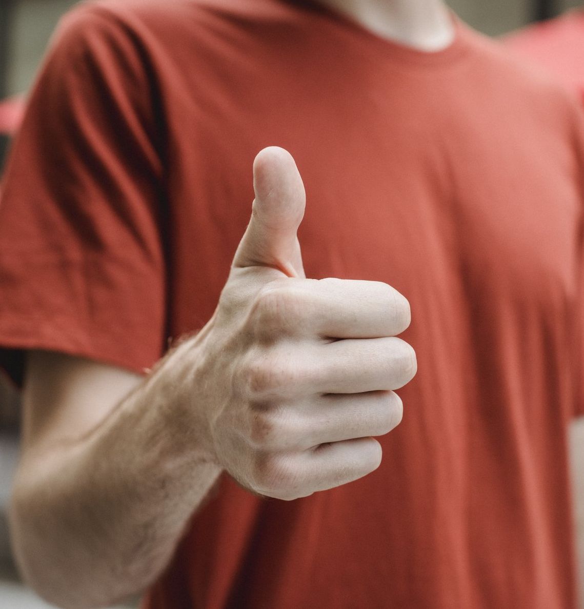 Close-up of a person in a red shirt giving a thumbs-up gesture