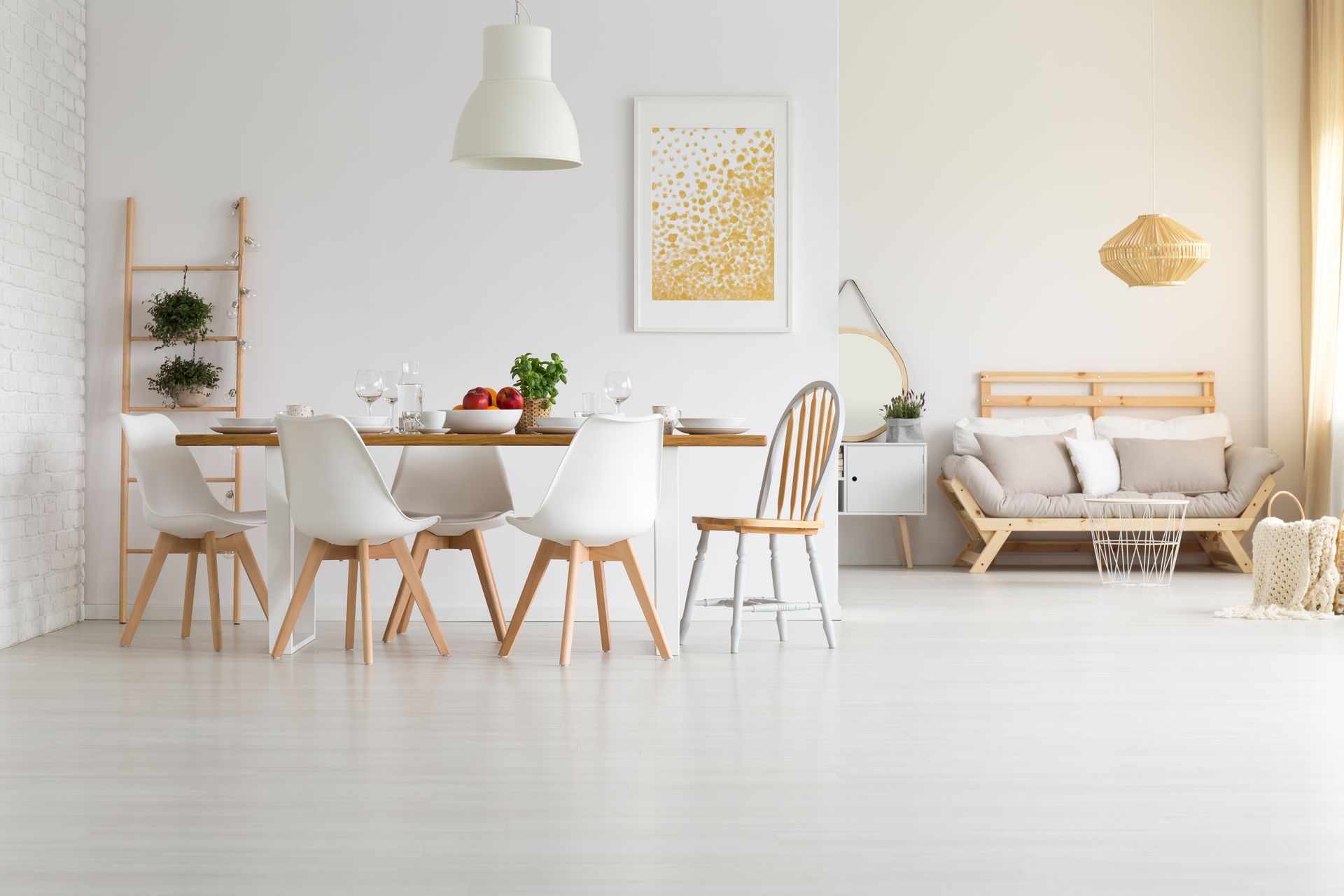 Bright minimalist dining room with white chairs, wooden table, sofa, and hanging lamp