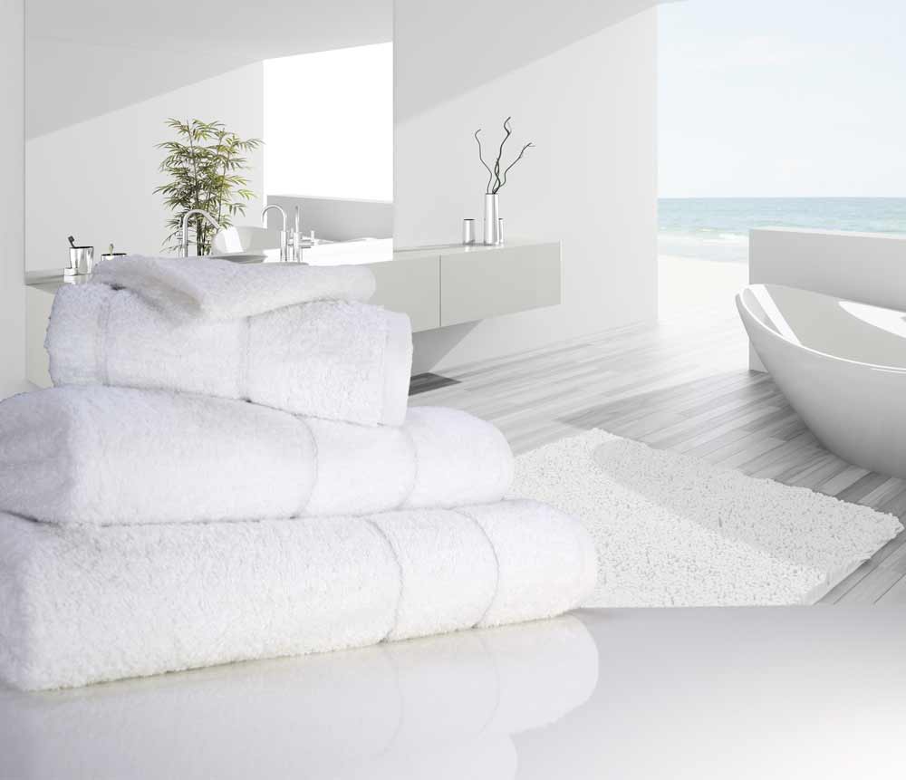 Nicely folded white coloured 700 gsm Eqyptian quality cotton towels next to a bathtub