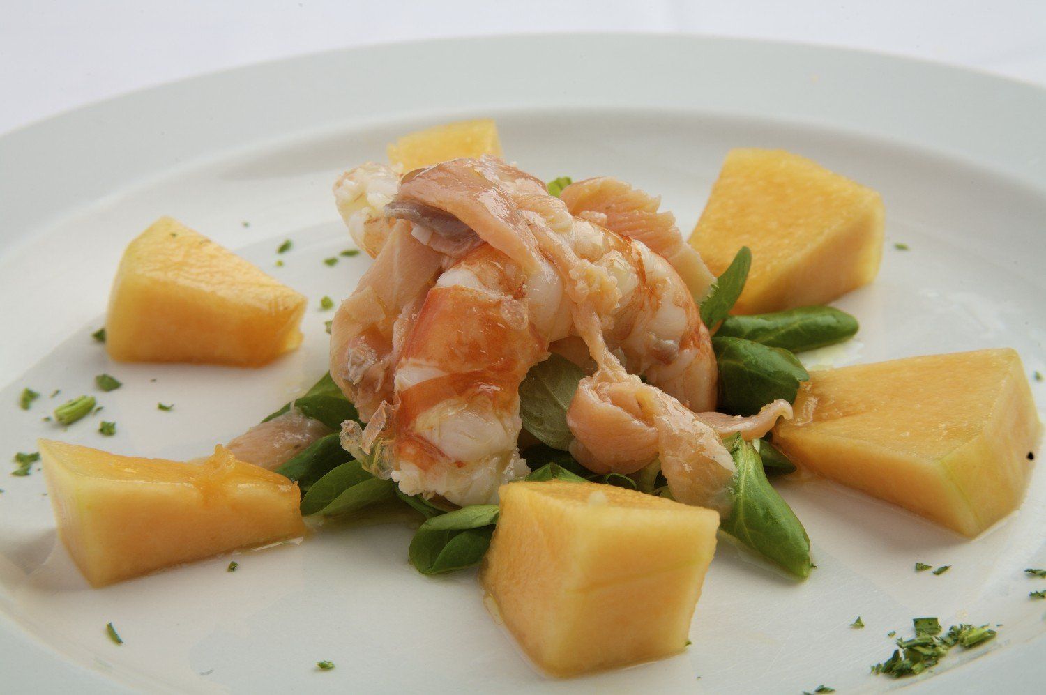 Piatto di gamberi con pezzi di melone e fagiolini su un piatto bianco.