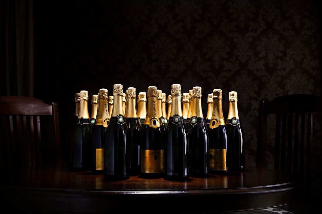 Bottiglie di champagne su un tavolo di legno scuro, coperchi in lamina dorata, parete decorata sullo sfondo.