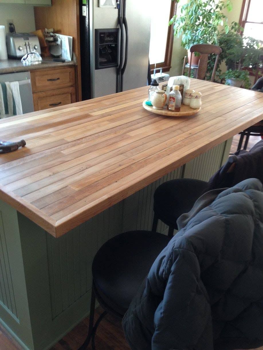 Wooden kitchen island with a fruit tray, chairs, and a coat draped over one seat in a bright kitchen.