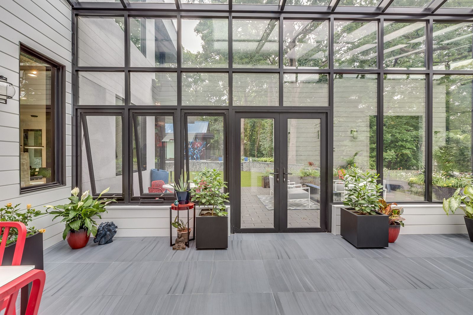 Glass lobby with double doors, potted plants, and red chairs on a gray floor