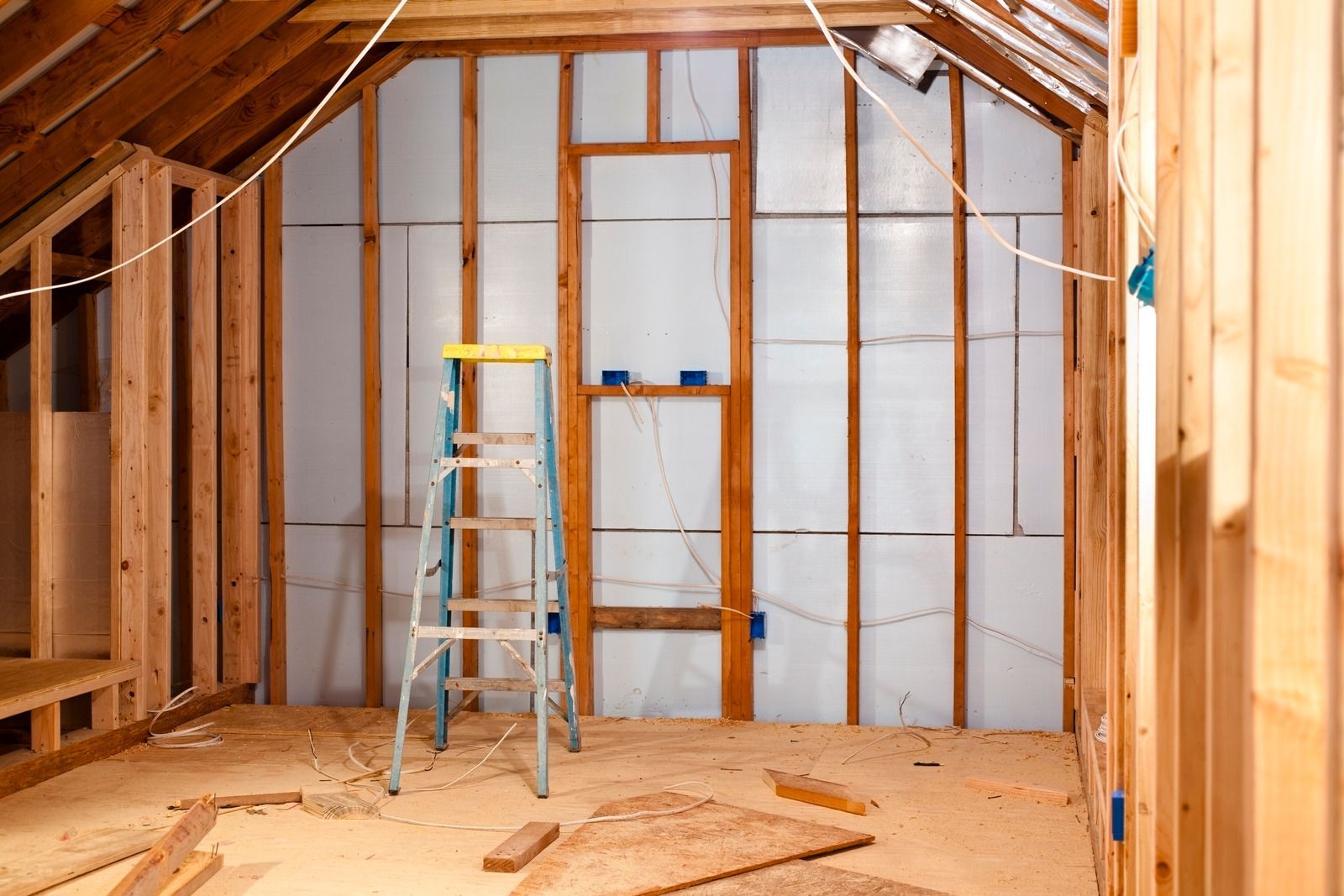 Interior of a framed attic under construction with a ladder and exposed insulation