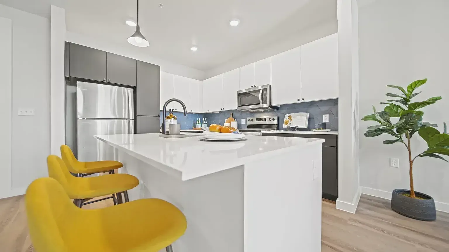 Modern kitchen with white countertops, stainless steel appliances, and bar stools.