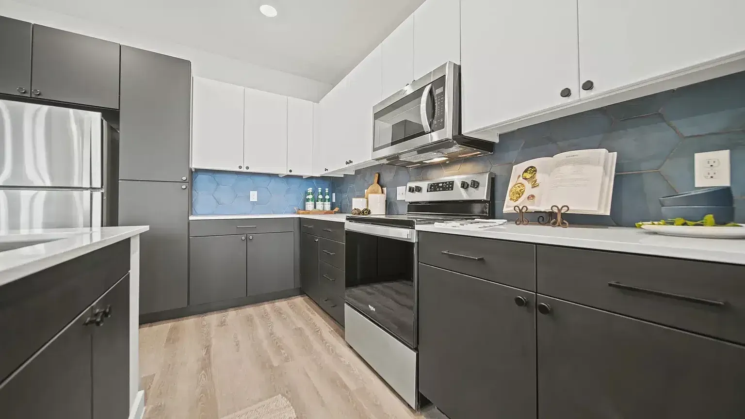 Modern kitchen with dark grey and white cabinets, stainless steel appliances, and a blue hexagonal tile backsplash.