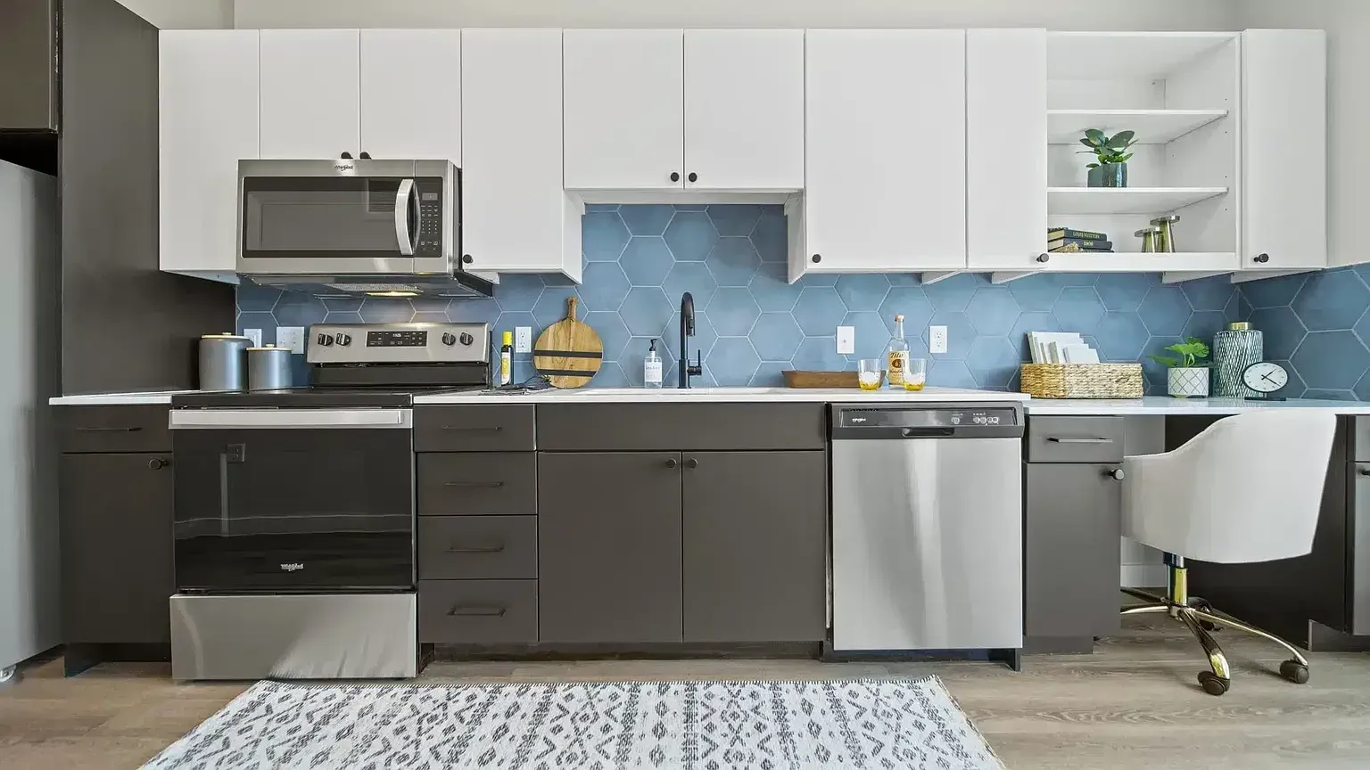 Modern kitchen with white upper cabinets, grey lower cabinets, stainless steel appliances, and blue hexagonal backsplash.