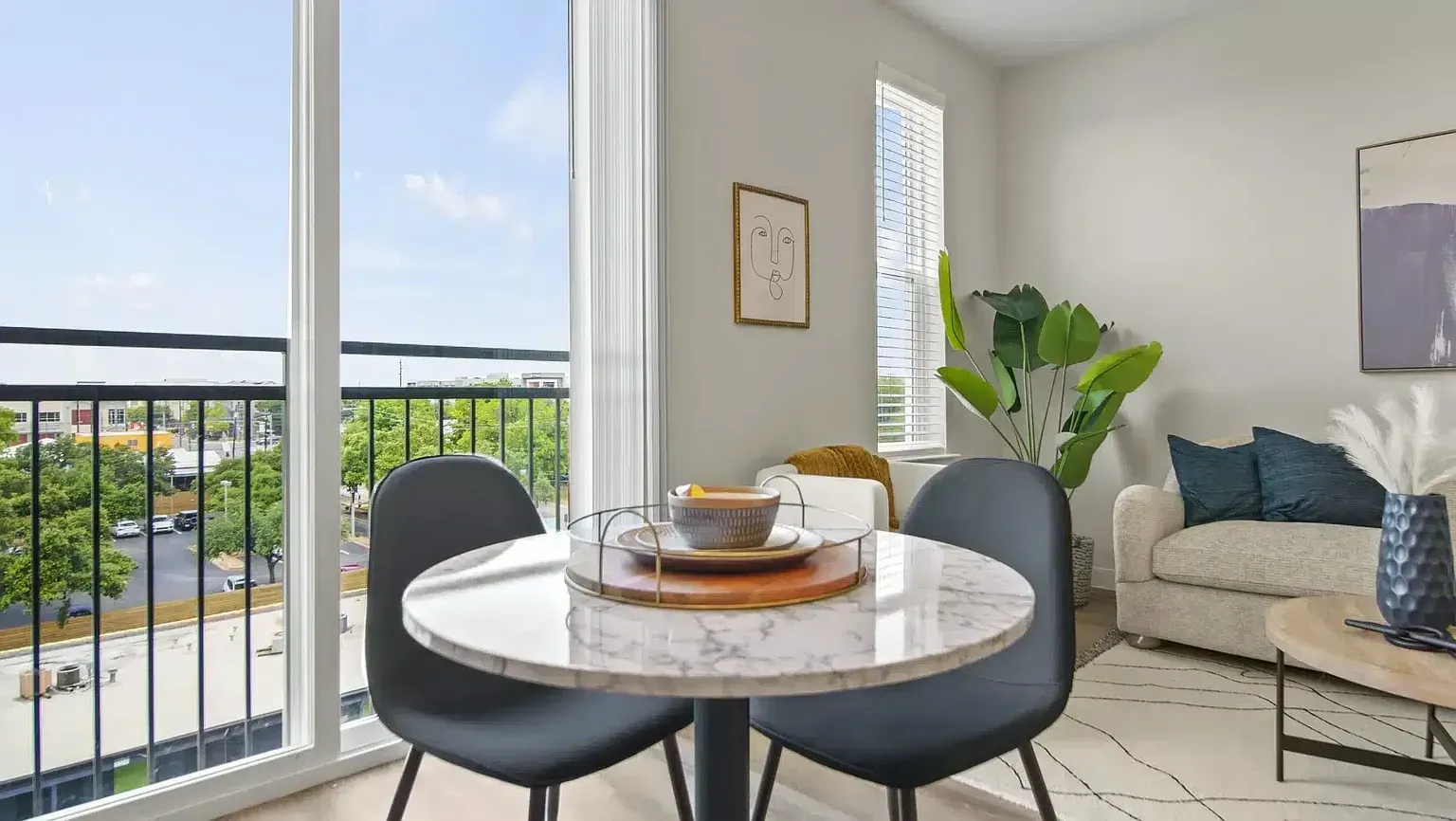 Dining area with marble table and chairs next to a balcony with city views.