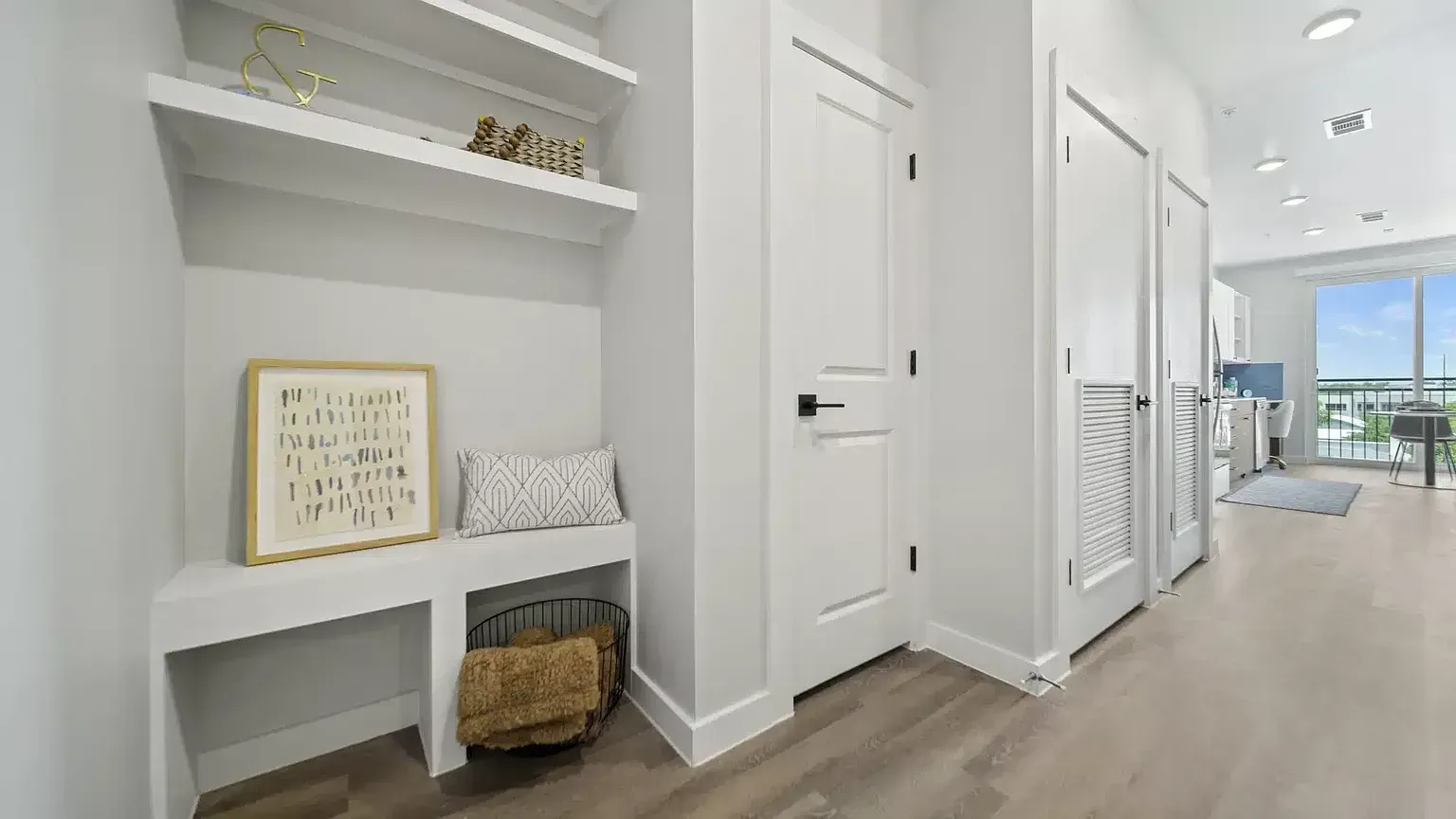Entryway with built-in shelving, bench, and decorative items. Doors and view of a home office.