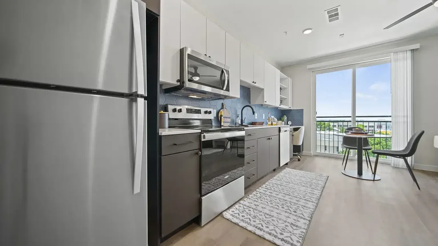 Modern apartment kitchen with stainless steel appliances, gray cabinetry, and a small dining area.