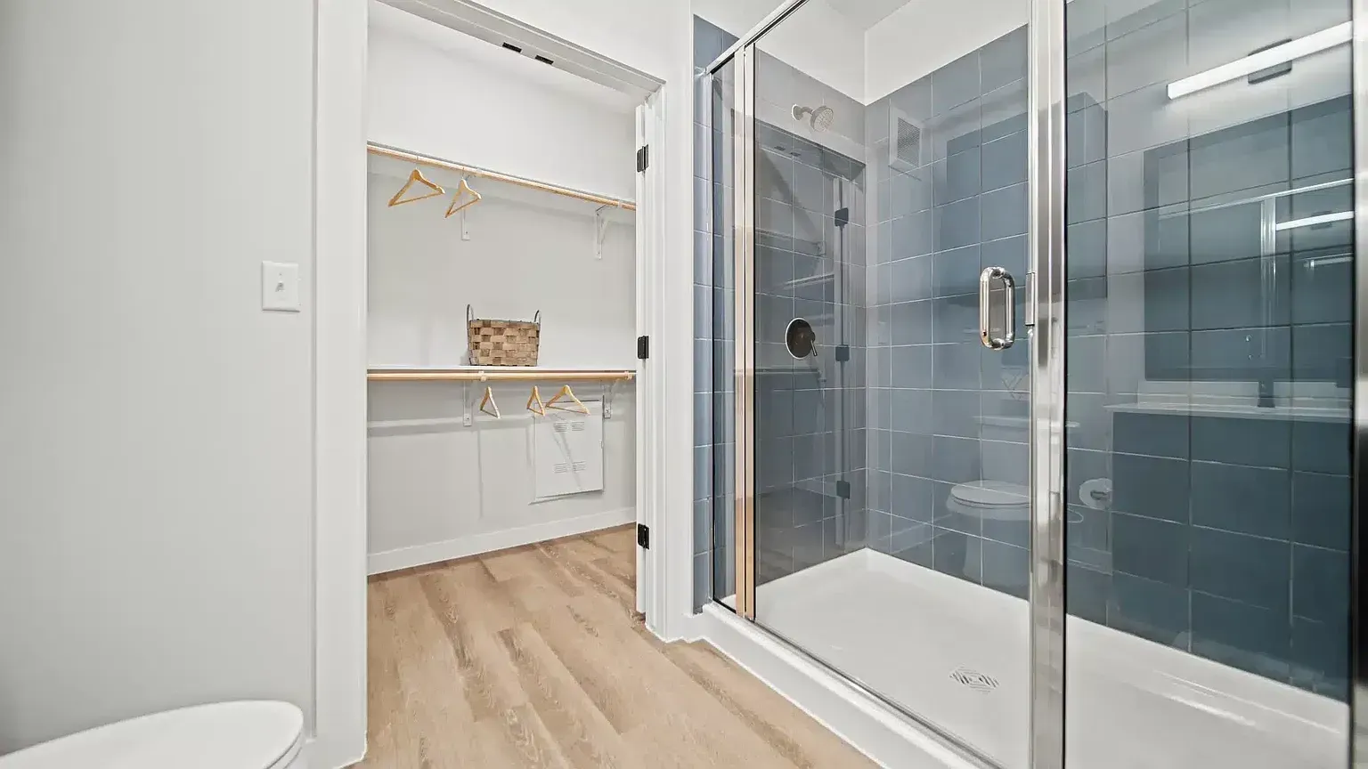 Walk-in closet and glass-enclosed shower with blue tile in an apartment bathroom.