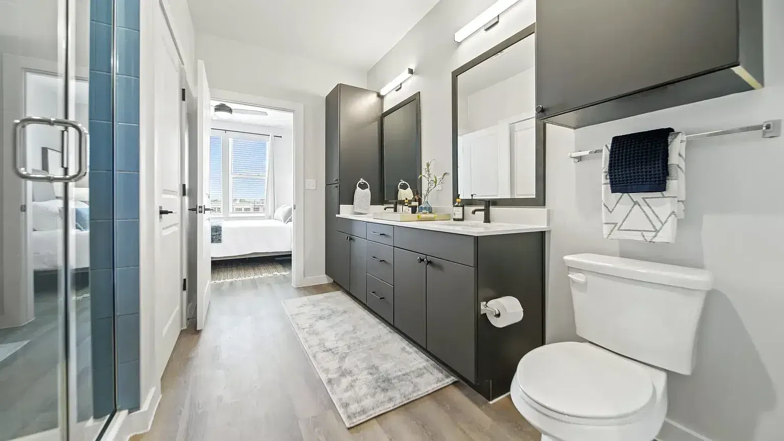 Modern bathroom with double vanity, walk-in shower, and view into a bedroom.