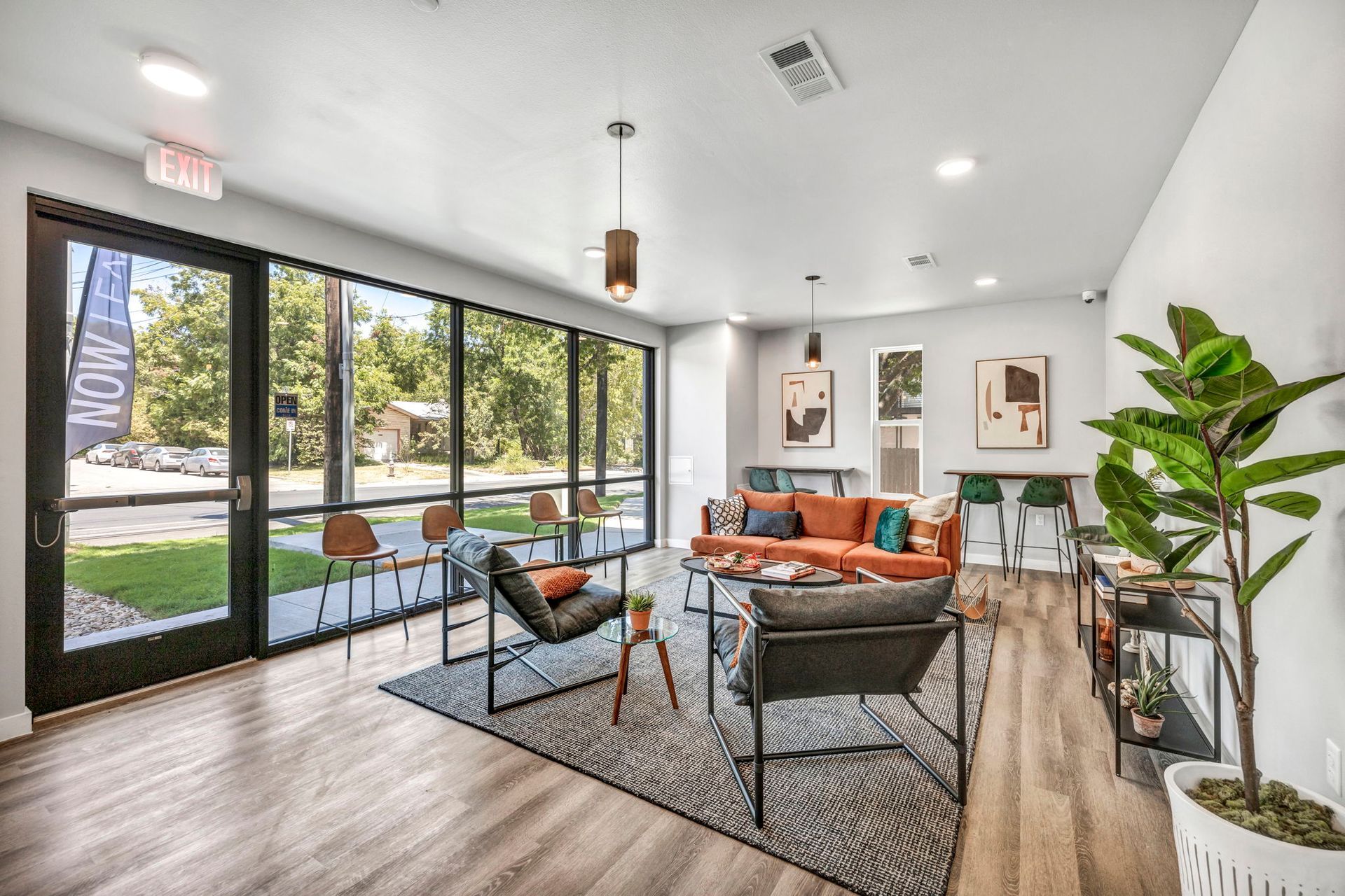 Bright modern lounge with orange chairs, large windows, wood floors, and a potted plant