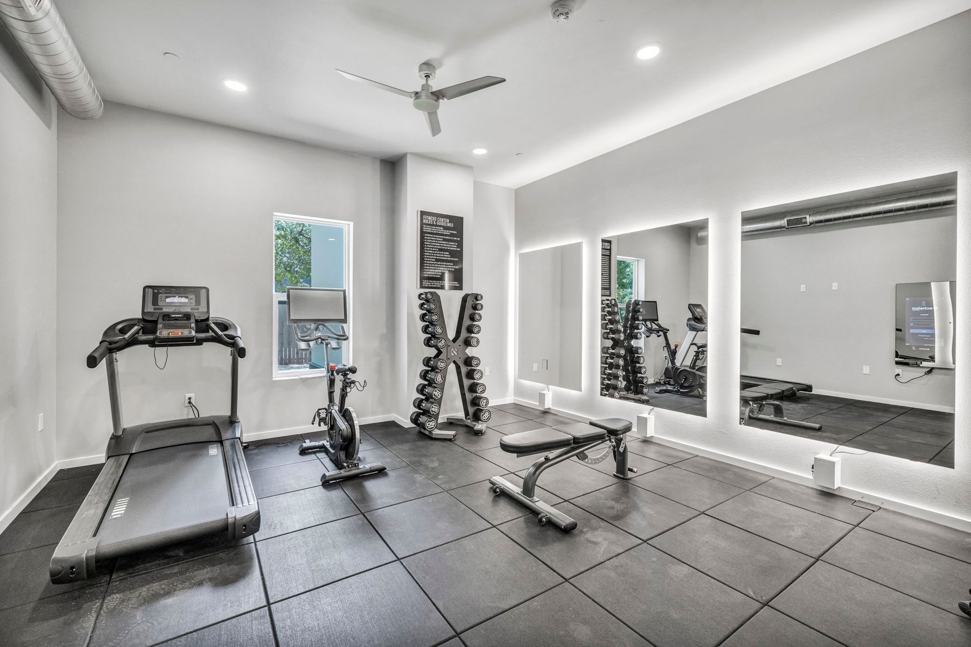 Modern home gym with treadmill, weights, bench, mirrors, and gray tiled floor