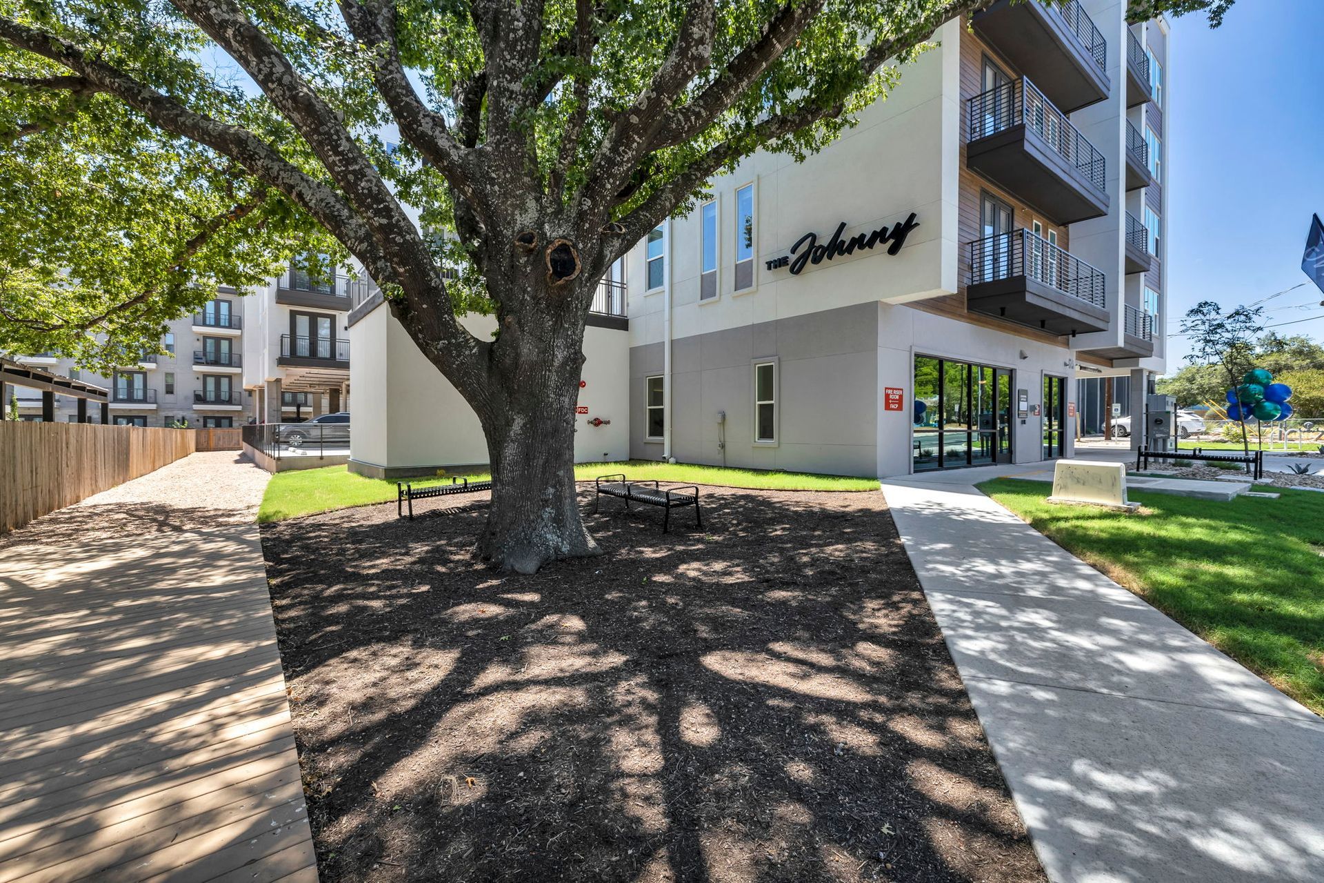 Modern apartment building entrance with large tree, sidewalk, and landscaped courtyard