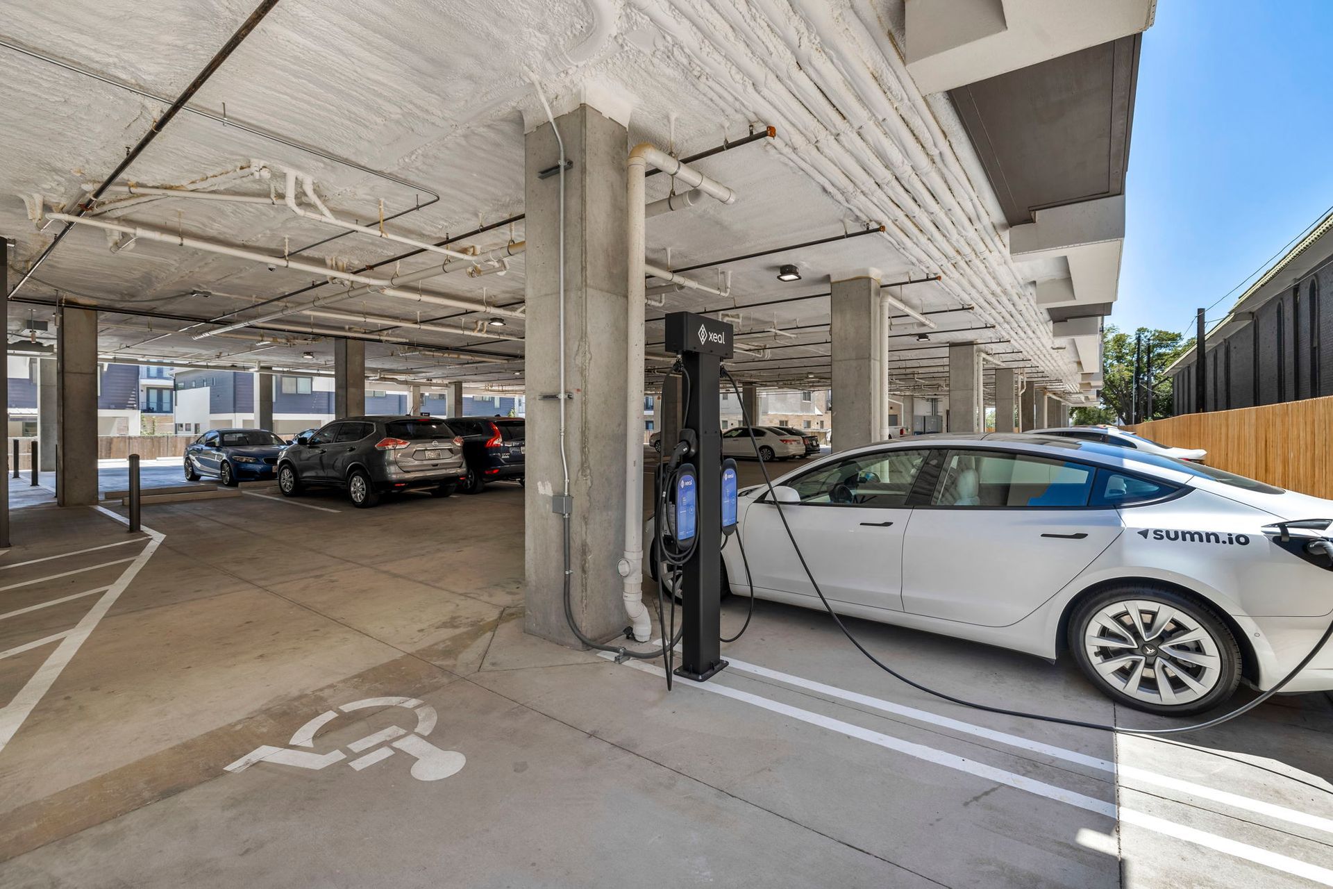Covered parking garage with cars, a concrete pillar, and a white car charging at an EV station.