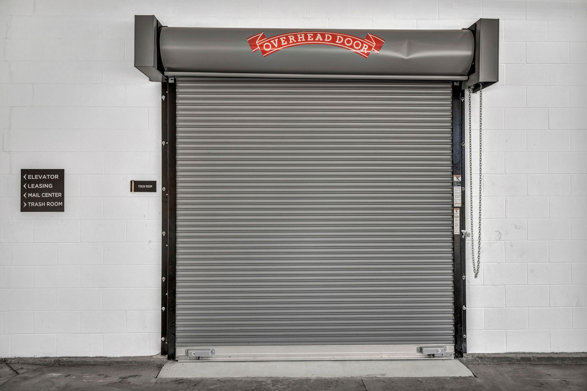 Closed gray metal roll-up garage door in a white tiled wall