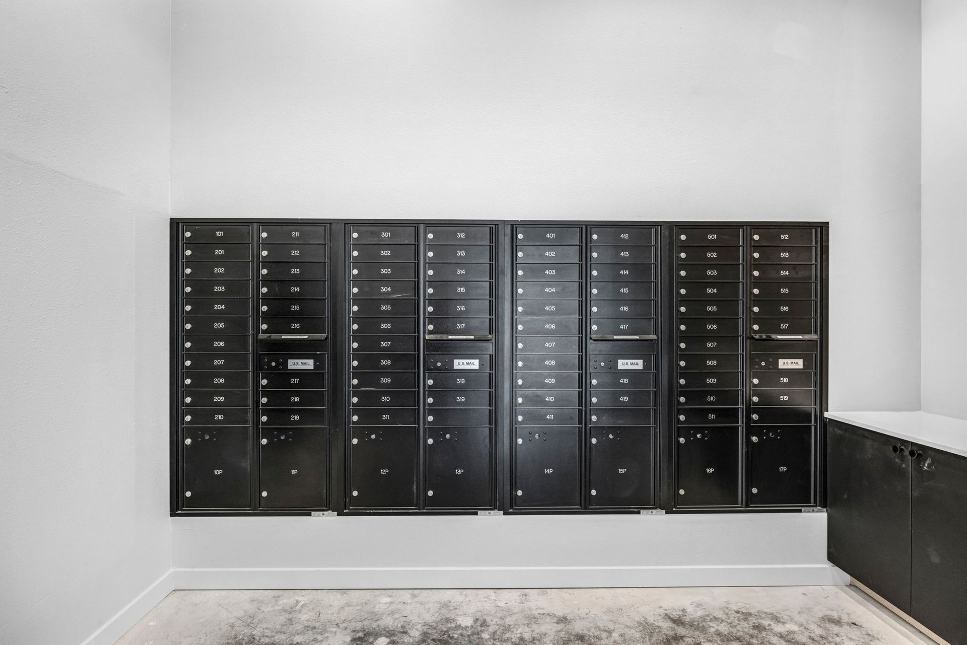 Black wall of mailboxes in a bright lobby or apartment mailroom